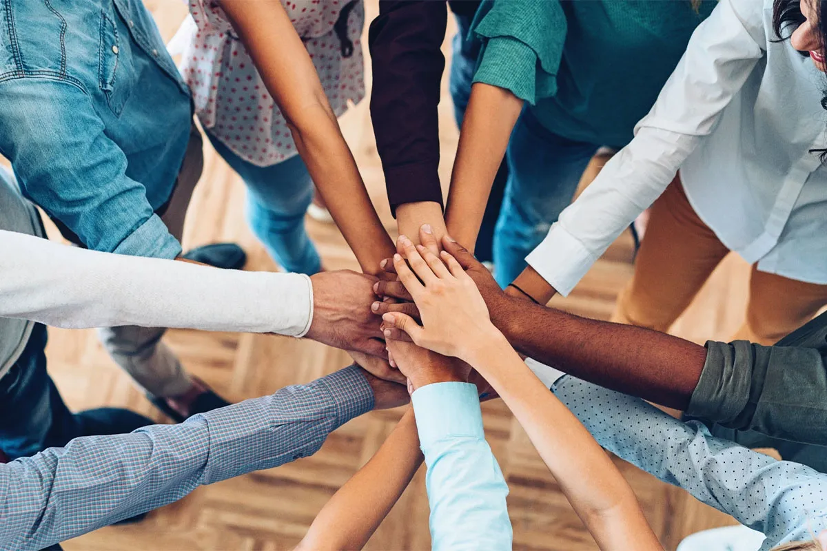 A group of people standing together in a circle with their hands together in the middle