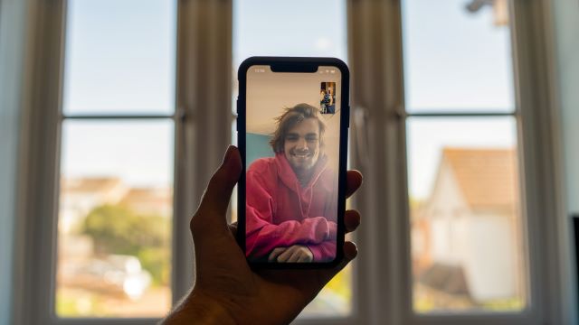 Image of an arm holding a phone, they are on a video call with another person, who we can see on the phone screen.